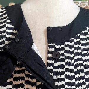 May include: Black and white striped blouse with a black collar and buttons. The blouse has a textured pattern.