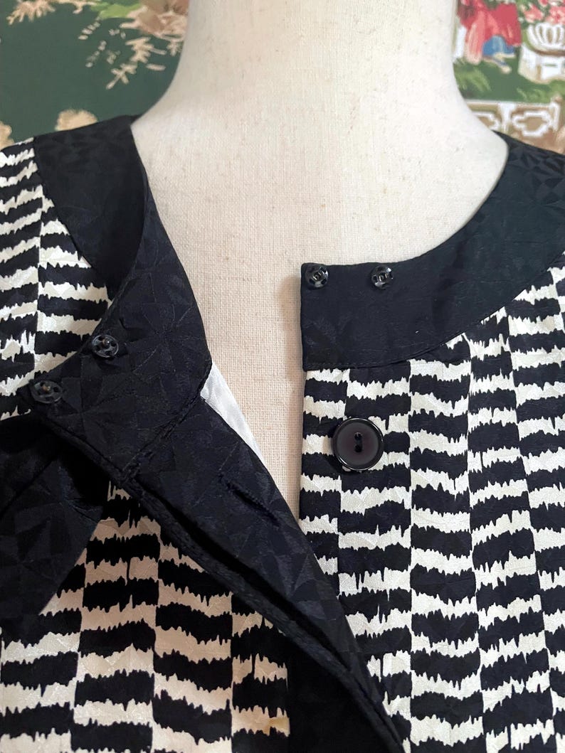 May include: Black and white striped blouse with a black collar and buttons. The blouse has a textured pattern.