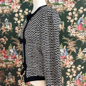 May include: A black and white striped cardigan with a black bow detail. The cardigan is on a white mannequin against a green and white floral patterned background.