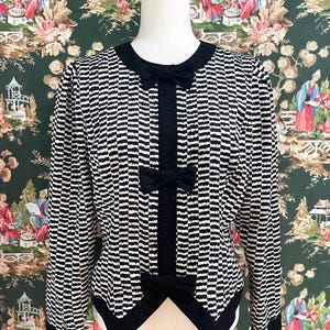 May include: A black and white striped jacket with a black bow at the neckline and black trim. The jacket has a fitted silhouette and long sleeves.