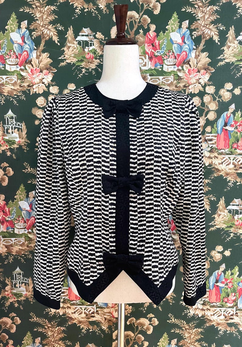 May include: A black and white striped jacket with a black bow at the neckline and black trim. The jacket has a fitted silhouette and long sleeves.