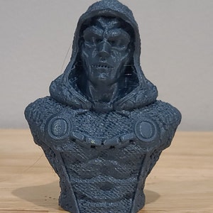 May include: A 3D printed bust of a character wearing a hooded cloak. The bust is gray and has a detailed face and clothing.