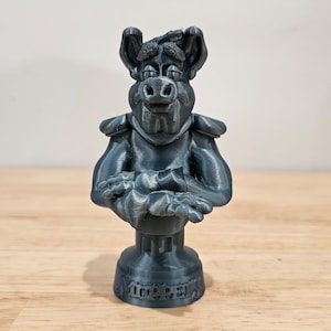 May include: A gray 3D printed bust of a cartoon character with a pig-like snout, wearing armor and holding its arms crossed. The base of the bust is inscribed with the words "Major  Press".