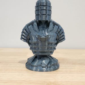 May include: A 3D printed bust of a character wearing a helmet and armor. The bust is gray and has a detailed design.