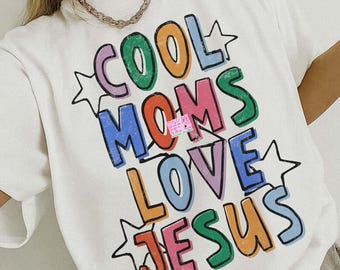 May include: White t-shirt with the text "COOL MOMS LOVE JESUS" in colorful, distressed lettering. The design includes star accents and is labeled "PNG SOLID & DISTRESSED". The shirt also has the text "ORIGINAL DESIGNER" on it.