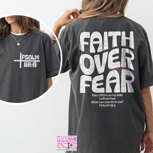 May include: A dark gray t-shirt with the text "FAITH OVER FEAR" in white with a distressed look. The text "The LORD is on my side; I will not fear What can man do to me? PSALM 118:6" is printed in white below the main text. The shirt also has a small logo on the bottom left corner.