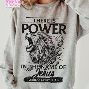 May include: A gray sweatshirt with a black and white graphic design of a lion breaking free from chains. The text "There is Power in the name of Jesus to break every chain" is printed on the sweatshirt.