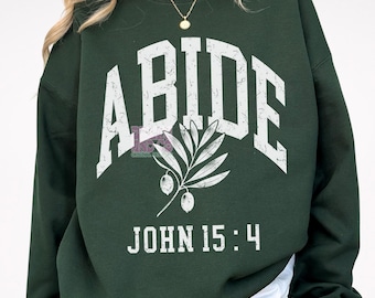 May include: Green sweatshirt with the word "ABIDE" in white distressed lettering, an olive branch design, and the text "JOHN 15:4" in white distressed lettering.