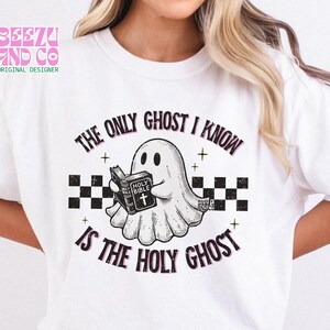 May include: A white t-shirt featuring a graphic of a ghost holding a book labeled Holy Bible. The text reads The Only Ghost I Know Is The Holy Ghost. The design includes a black and white checkered pattern, small star accents, and a distressed texture.