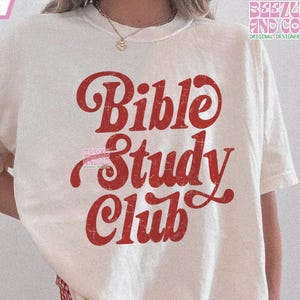 Op de afbeelding: Een wit T-shirt met een rode, verweerde afbeelding met de tekst "Bible Study Club".
