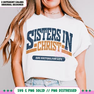 May include: White t-shirt with a blue and orange graphic that says "Sisters in Christ - Are Sisters for Life".
