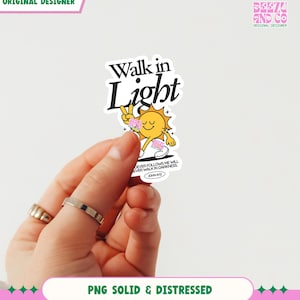 May include: A sticker with the text "Walk in Light" above a cartoon sun character giving a peace sign. The sticker also includes the text "DEVER FOLLOWS ME WILL EVER WALK IN DARKNESS JOHN 8:12". The sticker is held by a hand.