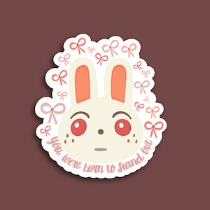 Pode incluir: Um coelho branco com olhos vermelhos e laços rosa em volta da cabeça. O texto "You were born to stand out" está escrito abaixo do coelho.