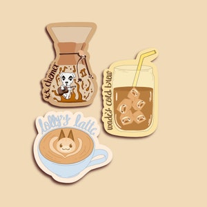 以下が含まれることがあります： コーヒーをテーマにしたイラストが描かれたステッカーが3枚。最初のステッカーには、ブラウンとホワイトのコーヒーメーカーに「**k.k. chemex**」の文字と、ギターを持った漫画の犬が描かれている。2枚目のステッカーには、グラスに入ったアイスコーヒーに「**wade's cold brew**」の文字とストローが描かれている。3枚目のステッカーには、ラテアートが描かれたカップに「**lolly's latte**」の文字と、泡の中に漫画の猫の顔が描かれている。