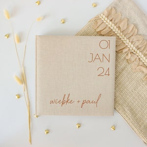 Può includere: Un album di nozze in lino beige con la data "01 JAN 24" e i nomi "wiebke + paul" stampati in marrone.