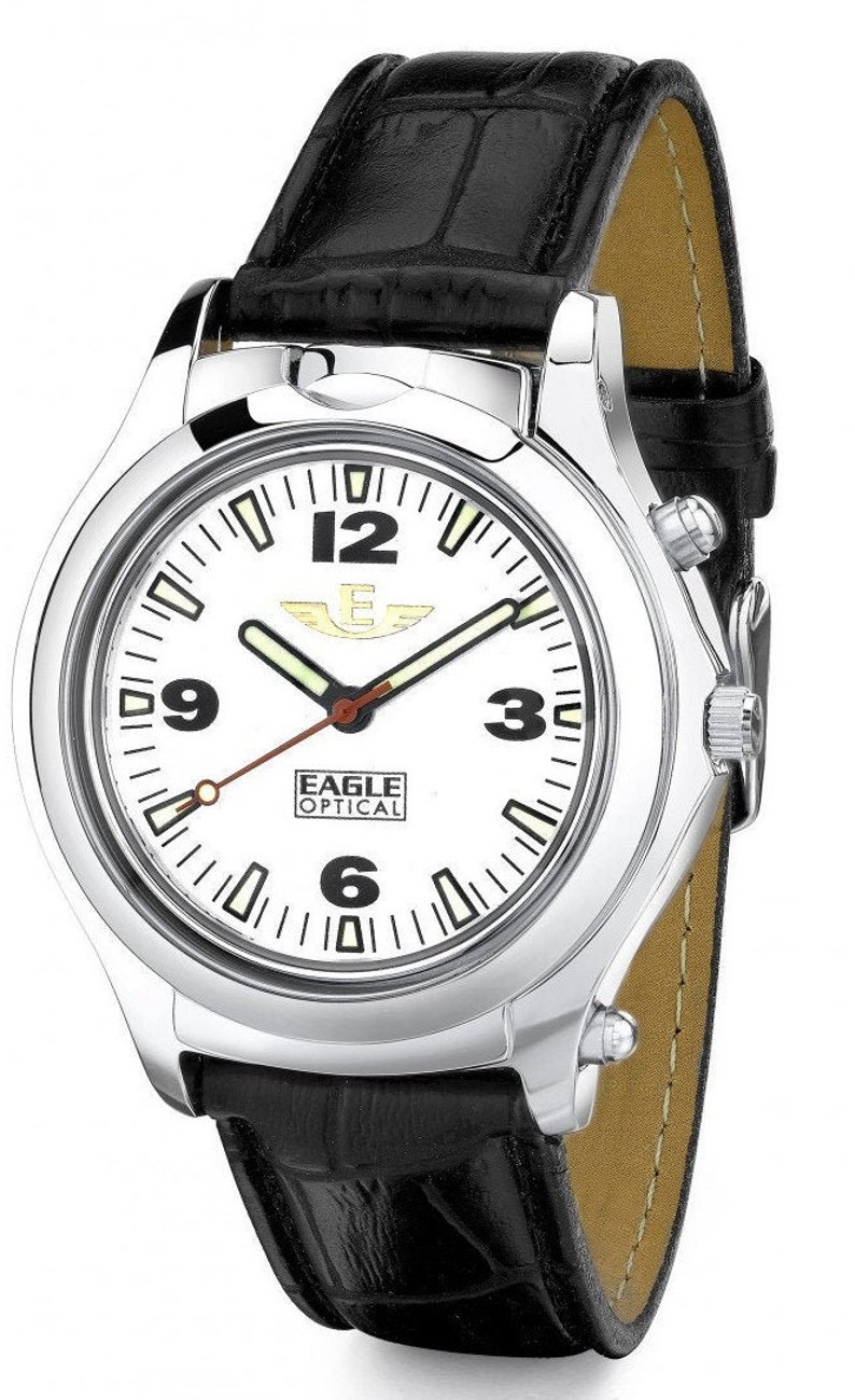 Puede incluir: Un reloj plateado con una esfera blanca y una correa de cuero negro. El reloj tiene una esfera grande y clara con n&uacute;meros y manecillas negros. La correa est&aacute; hecha de cuero genuino y tiene un patr&oacute;n de cocodrilo. La esfera del reloj tambi&eacute;n presenta el texto "Eagle Optical".