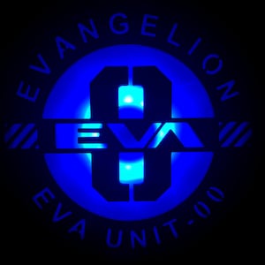May include: A blue and black circular logo with the text "EVANGELION" around the outside, "EVA" in the center, and "EVA UNIT-00" at the bottom. The number "0" is in the center of the logo.