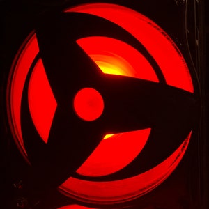 May include: A red and black circular design with a three-pointed star shape in the center. The design is illuminated from behind, creating a glowing effect.