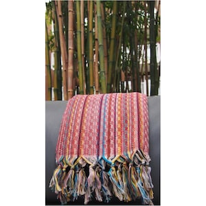 May include: A red, yellow, and blue striped Turkish towel with fringe. The towel is folded and draped over a gray couch.