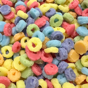 May include: A close-up of a bowl of colourful cereal rings. The cereal is a mix of yellow, pink, blue, and purple.