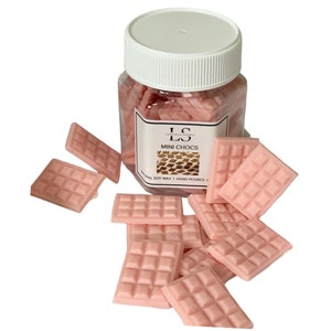May include: A glass jar filled with pink wax melts shaped like chocolate bars. The jar has a white lid and a label that says "LS Luxurious Scents MINI CHOCS NATURAL SOY WAX | HAND POURED".