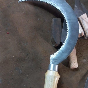 May include: A curved, serrated blade with a wooden handle. The blade has a Damascus steel pattern and is attached to the handle with a metal ring.