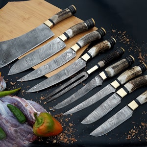 May include: Set of eight kitchen knives with patterned blades and stag horn handles. The knives include a cleaver, a carving knife, a chef's knife, a paring knife, and a fork.