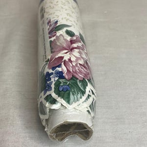 May include: A roll of floral wallpaper with a white background and a pink, blue, and green floral pattern. The wallpaper is packaged in a clear plastic sleeve.