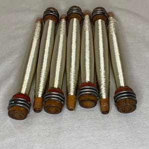 May include: Eight wooden spools with white thread wound around them. The spools have a red and silver band around the top.