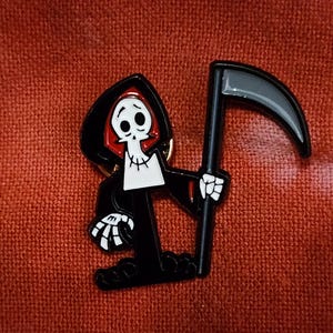 以下が含まれることがあります： 白い頭蓋骨、赤いアクセント、黒い大鎌を持つ漫画の死神キャラクターを特徴とする黒いエナメルピン。 ピンは、テクスチャ加工された赤い背景に設定されています。