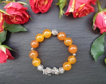 Op de afbeelding: Een armband gemaakt van oranje edelsteen kralen met zilveren accenten. De armband heeft een zilveren bedel in de vorm van een mythisch wezen.