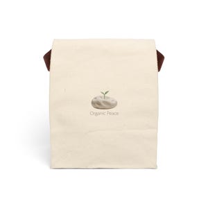 May include: A cream-coloured tote bag with dark brown handles. The front of the bag features a small illustration of a sprout growing from a stone, with the words "Organic Peace" printed below.
