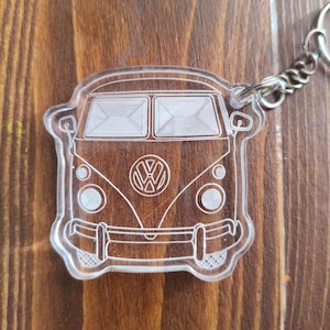 Op de afbeelding: Transparante acryl sleutelhanger met een gedetailleerde omtrek van een klassieke Volkswagen bus. De sleutelhanger heeft een zilverkleurige metalen ketting en ring. Het busontwerp bevat het VW-logo aan de voorkant.