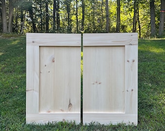 May include: Two unfinished, light wood cabinet doors with a raised panel design. The doors are sitting on a grassy surface.