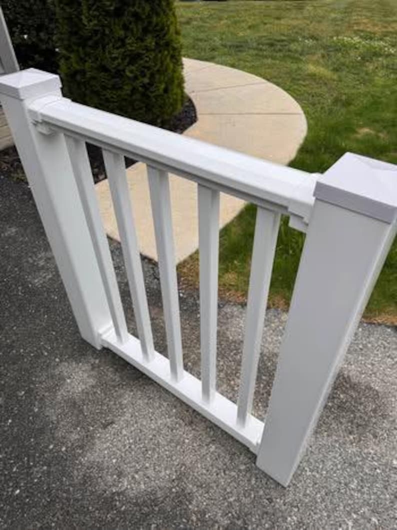 May include: A white vinyl railing section featuring two square posts with flat caps, a horizontal top rail, and a horizontal bottom rail connected by four vertical balusters. The structure is constructed from smooth, solid white material.