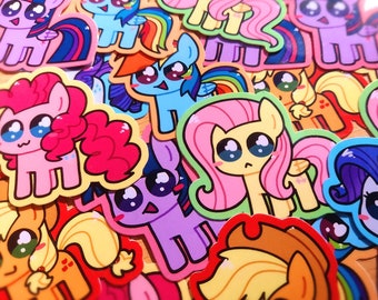 Könnte beinhalten: Eine Sammlung farbenfroher Cartoon-Pony-Aufkleber. Jeder Aufkleber zeigt einen anderen Pony-Charakter mit großen Augen und leuchtenden Farben, darunter Rosa, Blau, Lila und Gelb. Die Aufkleber haben eine glänzende Oberfläche und sind in einer Nahaufnahme überlappend angeordnet.