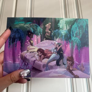 Könnte beinhalten: Ein farbenfroher Kunstdruck mit einer Gruppe von Meerjungfrauen in einer mystischen Umgebung. Die Illustration zeigt Meerjungfrauen mit verschiedenen Hauttönen und Haarfarben, die auf einer Felsformation liegen. Der Hintergrund umfasst üppiges Laub und ein Wasserelement, mit einem lila und türkisfarbenen Farbschema.