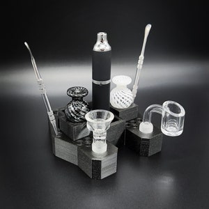 May include: A collection of glass smoking accessories, including a black vaporizer, dab tools, and glass bowls, arranged on a black hexagonal stand. The stand provides organized storage for the various components.