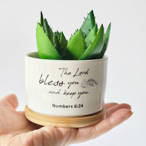 May include: White ceramic planter with a green succulent plant. The planter has the text "The Lord bless you and keep you. Numbers 6:24" printed on it.