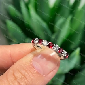 May include: A silver-toned band ring featuring an alternating pattern of round-cut red rubies and clear white diamonds. The stones are set in a row along the top half of the metal band, creating a continuous sparkling effect across the finger.