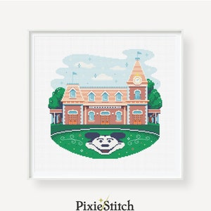 May include: A cross-stitch pattern featuring a pixelated illustration of a train station with Mickey Mouse's head in the foreground. The station is a light brown colour with a clock tower and a green roof. The sky is blue with white clouds and stars. The pattern is surrounded by a green border with swirls.