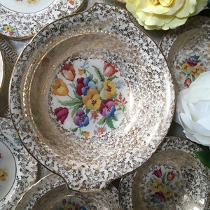 Puede incluir: Juego de cuencos de cerámica blanca vintage con ribetes dorados y diseños florales. Los cuencos presentan un patrón repetitivo de flores coloridas y acentos dorados.