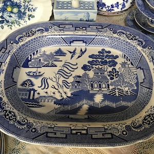 May include: A large oval blue and white porcelain serving platter with a traditional willow pattern. The platter features a detailed design of a Chinese landscape with trees, a bridge, and a pagoda.