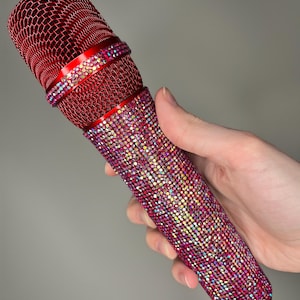 May include: A red microphone with a sparkly, iridescent rhinestone design. The microphone has a metal mesh grille and a black handle.