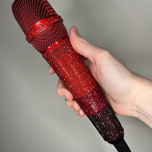 Op de afbeelding: Een rode microfoon bedekt met glinsterende rode strass steentjes. De microfoon heeft een zwarte basis.