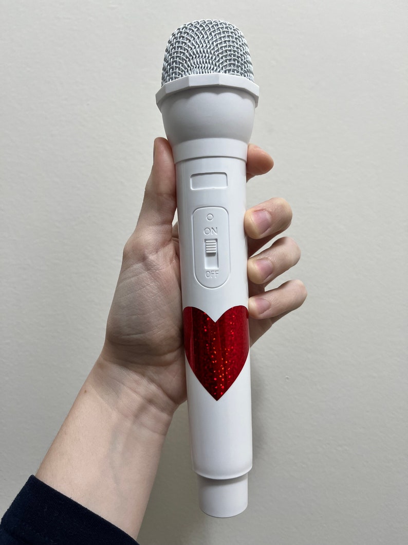 May include: White microphone with a red glitter heart sticker. The microphone has an on/off switch.