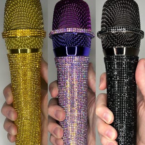 May include: Three microphones covered in rhinestones. The microphones are gold, purple, and black.