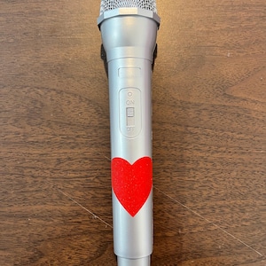 May include: A silver microphone with a red heart sticker on the body. The microphone has an on/off switch.