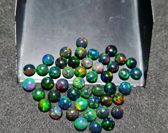 May include: A collection of black opal cabochons in various shades of green, blue, and red. The opals are displayed in a metal tray.