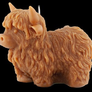 May include: A brown Highland cow figurine with detailed fur texture, horns, and a small tail. The figurine is a light brown color and is set against a black background. The cow is in a standing position.